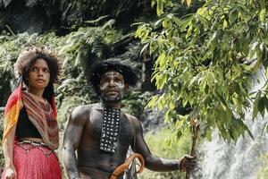 wamena, papúa, indonesia, 01 de junio de 2022 padre e hija de la tribu dani vestidos con ropa tradicional de pie juntos, contra la cascada en el bosque verde. familia papúa. foto