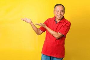 Portrait of cheerful Asian retired old man wears red t-shirt, pointing hands or presenting. photo