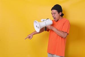 Asian casual guy isolated on yellow background shouting through a megaphone and pointing down finger. photo