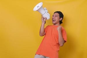 Asian man over isolated yellow wall shouting through a megaphone while celebrating success. Yes man. photo