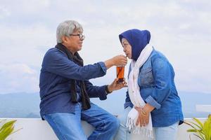 Romantic elderly couple. Old man giving drink to his wife in cafe. Happy retired couple photo