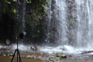 Modern camera is set on tripod for landscape photography in front of waterfall. photo