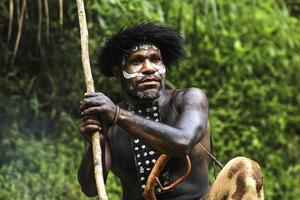 retrato de un hombre de la tribu dani vestido con koteka, ropa tradicional de papúa. hombres de la tribu dani mirando a su alrededor y listos para cazar presas animales en la jungla. foto