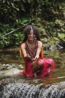 Wamena, Papua, INDONESIA, June 01, 2022 Attractive papua young girl  of dani tribe in traditional clothes is smiling and splashing water in the river. photo