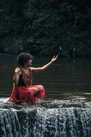 Wamena, Papua, INDONESIA, June 01, 2022 Young girl of a papuan tribe in traditional clothes is playing water in the river with waterfall photo