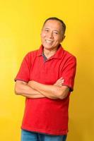 Portrait of Asian senior man wear red t-shirt with crossed arms isolated on yellow background. photo