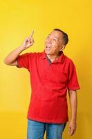 Wow, eureka, aha moment. Portrait of Asian senior man having great idea, pointing finger upwards, finding inspiration or solution to problem on yellow studio background. photo