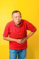 el anciano asiático mano en el estómago porque la enfermedad del dolor se siente mal, aislado en un fondo amarillo. foto