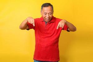 Asian senior man in red t-shirt smiling anf pointing finger down trying to pay attention to important information. photo