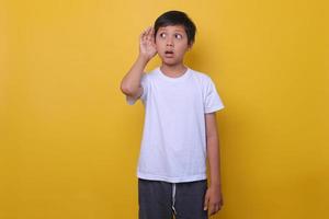 Asian boy in casual style listening at a distance, isolated on yellow background. Mock up for kids fashion. photo