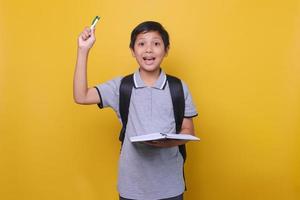 Portrait of an Asian school boy with an expression when he gets an idea or solution, wearing gray polo shirt and holding book and pen. Back to school concept. photo