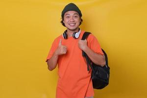Attractive Asian young man in casual student style is smiling and thumbs up, against yellow background. photo