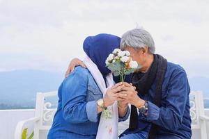 pareja romántica de ancianos besándose y cubriéndose la cara junto con una flor blanca. foto