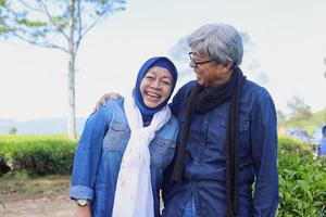 Happy elderly couple laughing at tea plantation. Old man hugging and looking his wife. Big smile white teeth. photo