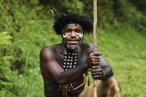 Potrait of Dani tribe man from Wamena Papua Indonesia wearing traditional clothes for hunting is smiling against blurred greenery forest background. photo