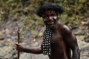 el retrato de un hombre de la tribu dani de wamena papua indonesia que usa ropa tradicional para cazar está sonriendo contra un fondo de bosque verde borroso. foto