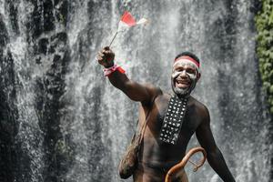 el hombre de papua de la tribu dani sonríe y celebra el día de la independencia de indonesia contra el fondo de la cascada. foto