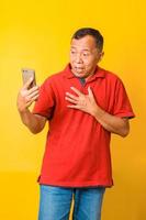 Portrait of surprised Asian senior man looking smart phone and being shocked, wide eyes and hand on chest. Human face expressions. Surprise, astonishment, wonder. photo