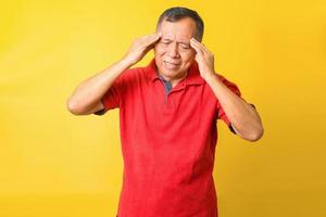 anciano asiático con camiseta informal sobre fondo amarillo que sufre de dolor de cabeza y está estresado por el dolor y la migraña. manos en la frente. foto