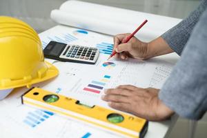 Asian engineer with architectural house plan project blueprint, graph and yellow helmet and engineering construction tools. photo