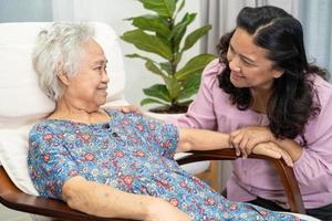 Asian elderly woman sitting relaxing with caregiver in rocking chair at room in home. photo