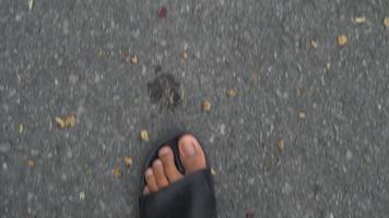 Video 4K. Above view of movement of the feet of a man in black sandals walking on the asphalt.