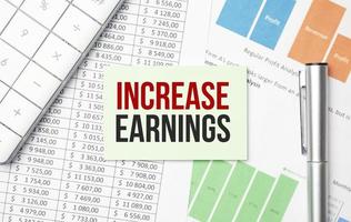 increase earnings words on business card and pen, calculator and charts photo