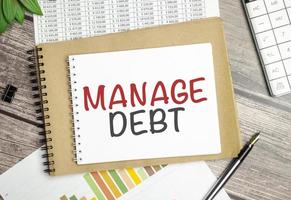 Text Manage Debt on notepad and pen on wooden background photo