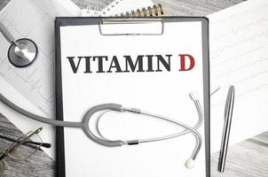 Text VITAMIN D on notebook with stethoscope and pen on wooden background photo