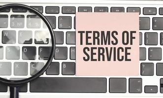 Terms of service words on pink sticker and magnifier on laptop photo