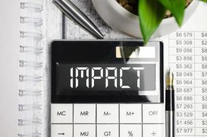 On the desktop there are reports, a white calculator with the text IMPACT on the scoreboard and a pen. Business concept. photo
