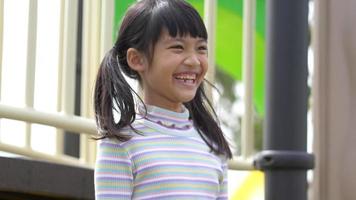 toma de mano, retrato de una encantadora chica asiática de pie mirando hacia adelante y riéndose con diversión en el patio de recreo video
