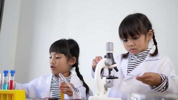 tir au ralenti, deux frères et sœurs asiatiques portant un manteau à l'aide d'un microscope pour expérimenter des liquides, tout en étudiant la chimie scientifique