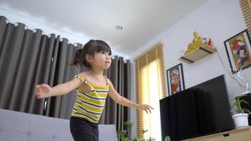 una chica encantadora practica desde una tableta con una pierna parada y manteniendo la pose de equilibrio en la sala de estar en casa
