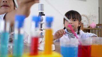 Selective focus at Asian little girl wearing coat using dropper to suck liquid from glass beaker, blur three colors liquids in beakers, while studying science chemistry video