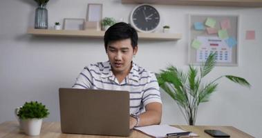 retrato de feliz hombre de negocios asiático cierra la computadora portátil y sale después de terminar de trabajar en la computadora portátil en la oficina en casa. cuaderno de cierre de freelancer exitoso. video