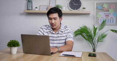 retrato de un hombre de negocios asiático feliz con una computadora portátil trabajando en la oficina en casa y recibiendo buenas noticias por correo electrónico. el alegre ganador masculino disfruta del éxito en la oficina en casa. video