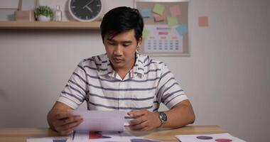 Portrait of Focused Asian businessman looks growth of sales secretary sorts documents in home office. video