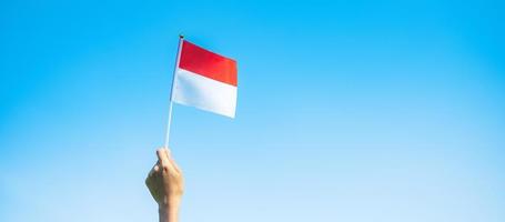 mano que sostiene la bandera de indonesia sobre fondo de cielo azul. día de la independencia de indonesia, día festivo nacional y conceptos de celebración feliz foto