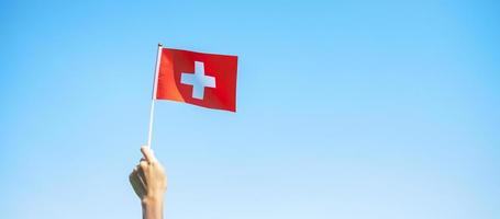 mano que sostiene la bandera suiza sobre fondo de cielo azul. día nacional de suiza y conceptos de celebración feliz foto