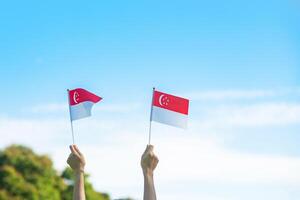 mano sosteniendo la bandera de singapur sobre fondo de cielo azul. día nacional de singapur y conceptos de celebración feliz foto