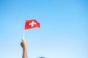 mano que sostiene la bandera suiza sobre fondo de cielo azul. día nacional de suiza y conceptos de celebración feliz foto