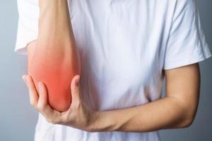 Young adult female with her muscle pain on gray background. Woman having elbow ache due to lateral epicondylitis or tennis elbow. injuries and medical concept photo