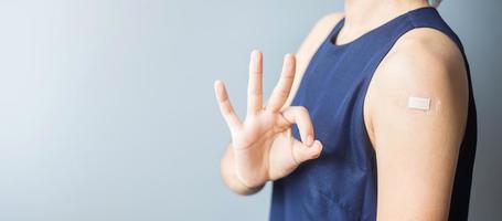 Happy woman showing OK sign with bandage after receiving covid 19 vaccine. Vaccination, herd immunity, side effect, efficiency, vaccine passport and Coronavirus pandemic photo