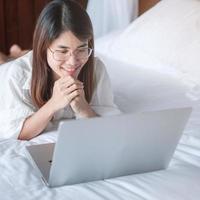 Happy woman using laptop for work, female meeting  online by computer notebook on bed. technology, network, work from home, lifestyle and digital communication concept photo