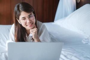 Happy woman using laptop for work, female meeting  online by computer notebook on bed. technology, network, work from home, lifestyle and digital communication concept photo