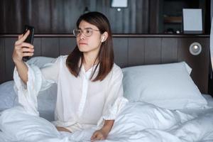 Happy woman using smart phone for video call, female meeting  online by mobile phone on bed. technology, network, work from home, lifestyle and digital communication concept photo