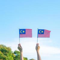 mano que sostiene la bandera de malasia sobre fondo de cielo azul. septiembre día nacional de malasia y agosto día de la independencia foto