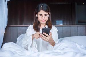 Happy woman using smart phone for video call, female meeting  online by mobile phone on bed. technology, network, work from home, lifestyle and digital communication concept photo