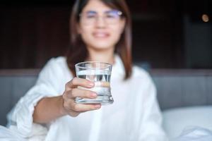 Happy woman holding water glass, female drinking pure water on bed at home. Healthy, Refreshment, lifestyle concept photo